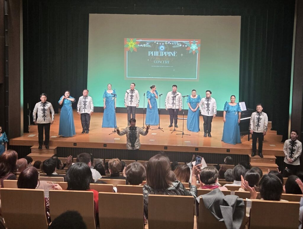 Counselor Celio Moniz of Timor-Leste attending the Philippine Christmas Concert in Tokyo, with performers from the UST Singers and Filipino artists on stage.