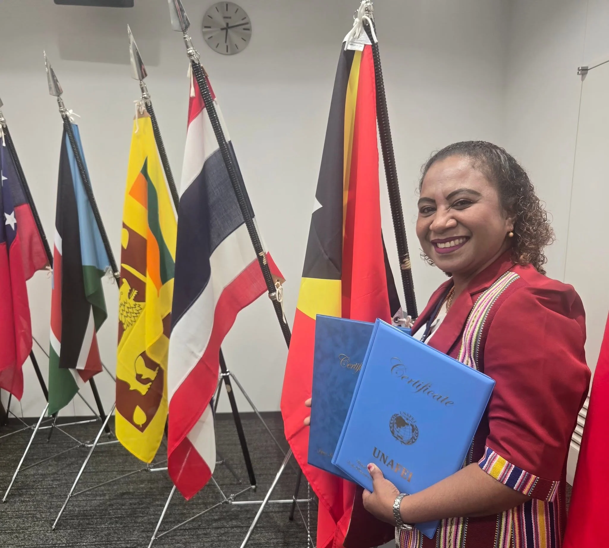 Ms. Lucia de Jesus Martins holding the UNAFEI Certificate before the national flags